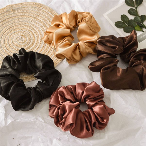Satin scrunchies in caramel, black and brown arranged on a woven mat
